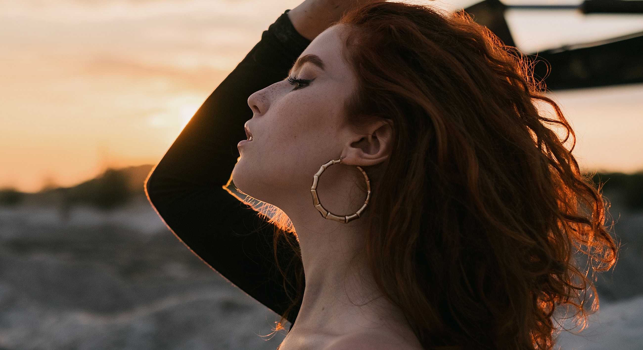 Woman with curly hair at sunset, wearing earrings.
